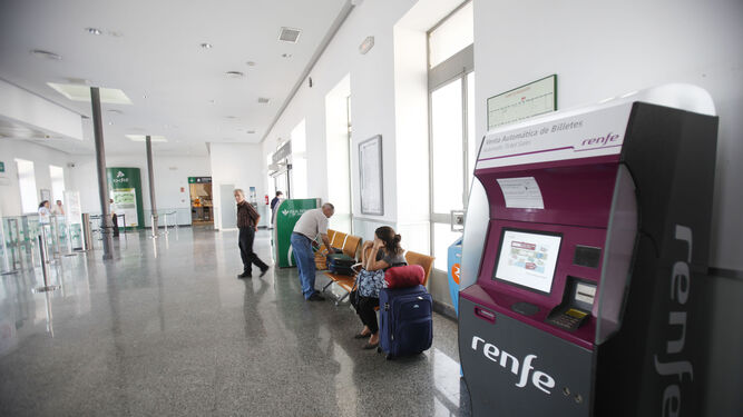 Pasajeros esperan en una estación de Adif junto a un dispensador de billetes de Renfe.