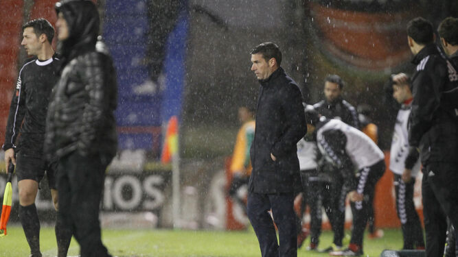 Luis Carrión sigue el partido desafiando a la lluvia desde la zona técnica del Anxo Carro, con Luis César Sampedro y el asistente en primer plano.