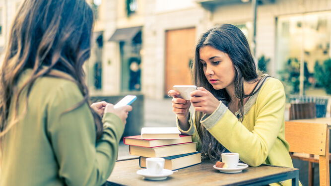 Dos chicas toman café mientras usan sus 'smartphones'.