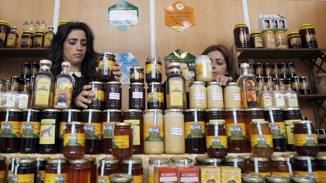 Dos mujeres colocan botes de miel en un expositor durante una edición de la feria Expomiel.