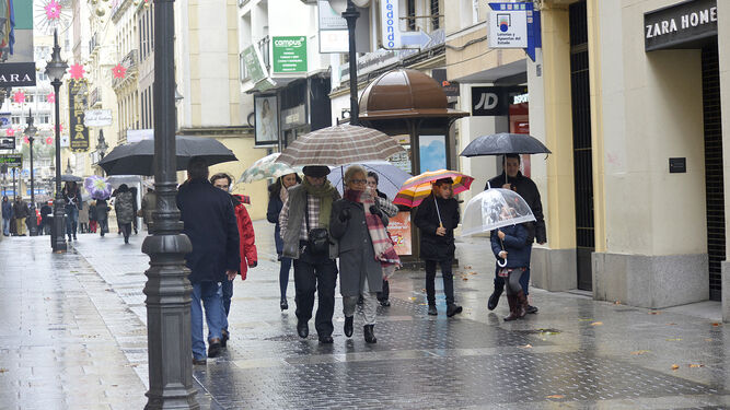 Un grupo de personas camina por la calle comercial Gondomar paraguas en mano.