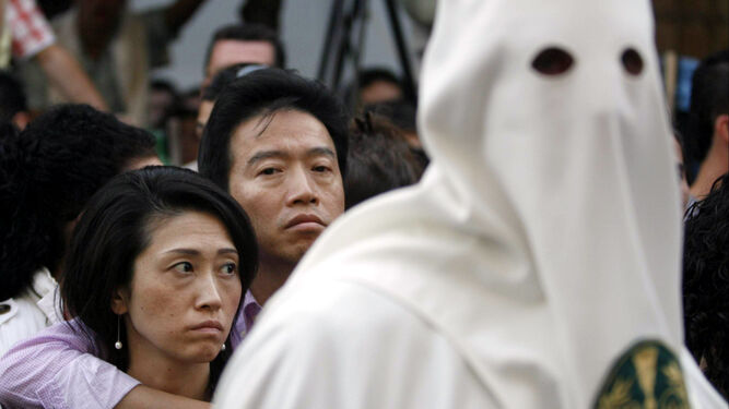 Dos turistas asiáticos observan la procesión de la hermandad de la Paz.