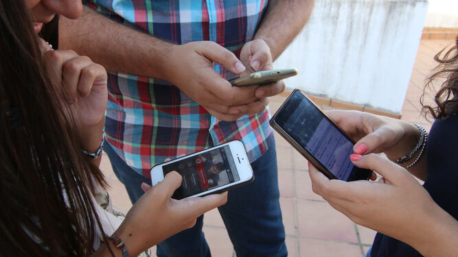 Tres jóvenes consultan su teléfono móvil.