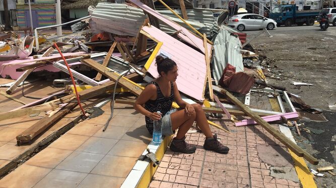 Imagen de Sara Cerezo sentada con una botella de agua junto a restos de viviendas tras el pasado del huracán.