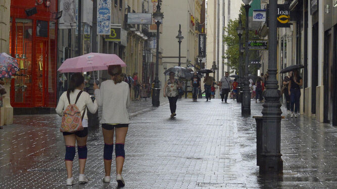 Dos jóvenes caminan bajo un paraguas, ayer en la calle Gondomar.
