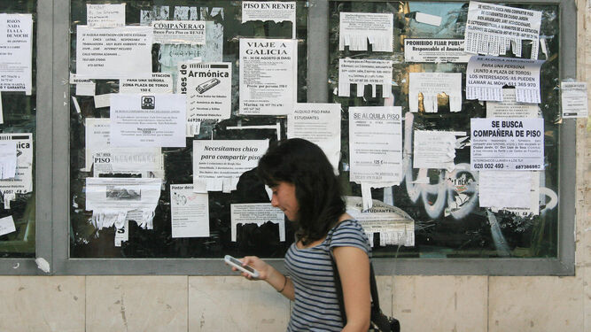 Una joven pasa delante de una pared con anuncios de alquiler de pisos.