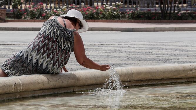 Una mujer se refresca en una fuente de Sevilla.