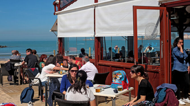 Varios clientes disfrutan de la terraza de un chiringuito en un día soleado.