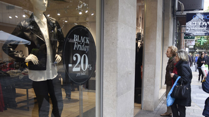 Dos señoras observan el escaparate de una tienda donde ya pueden verse los anuncios de descuentos por el Black Friday.