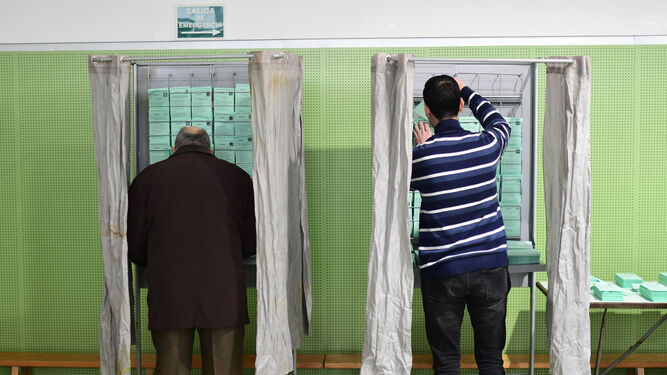 Dos personas cogen las papeletas para votar en un colegio electoral de la capital.