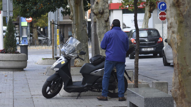 Un hombre espera junto a su moto, en la zona donde la Policía prohíbe aparcar.