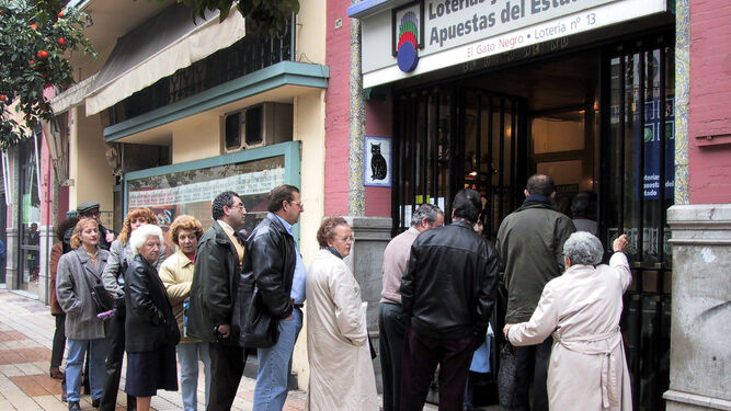 Varios sevillanos guardan cola frente a la administración de lotería El Gato Negro.