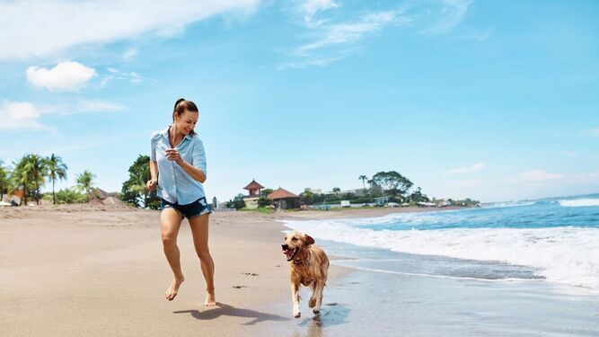 Una mujer corre por la playa acompañada de su perro.