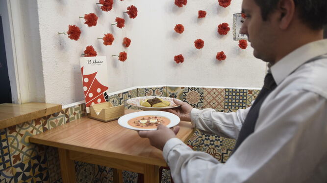 Un camarero de El Abanico sirve salmorejo y rabo de toro, platos típicos de la ciudad.