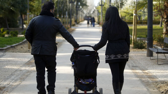 Una pareja camina por un parque con un cochecito de bebé.