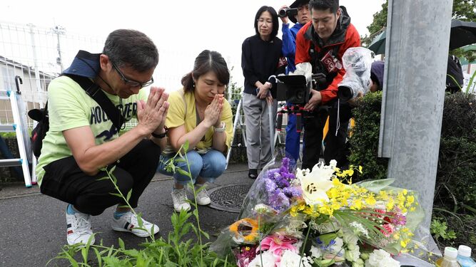 Varias personas rezan y depositan flores en los aledaños del edificio incendiado en Kioto.