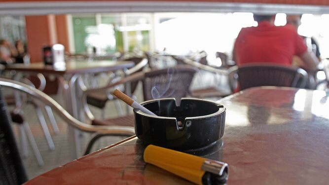 Un cigarrillo encendido en un cenicero en la mesa de una terraza de un bar.