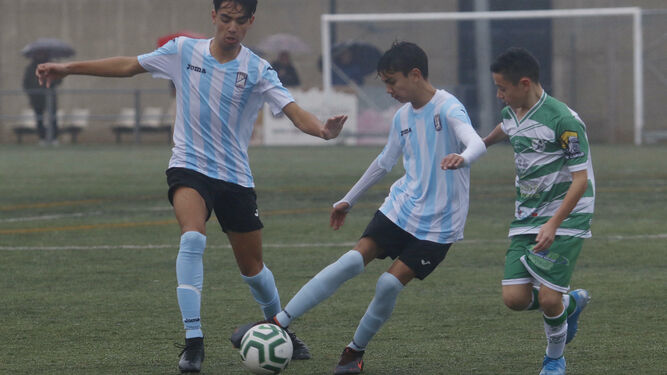 Un jugador del Don Bosco controla el esférico en presencia de un compañero y un rival del Juanín y Diego.