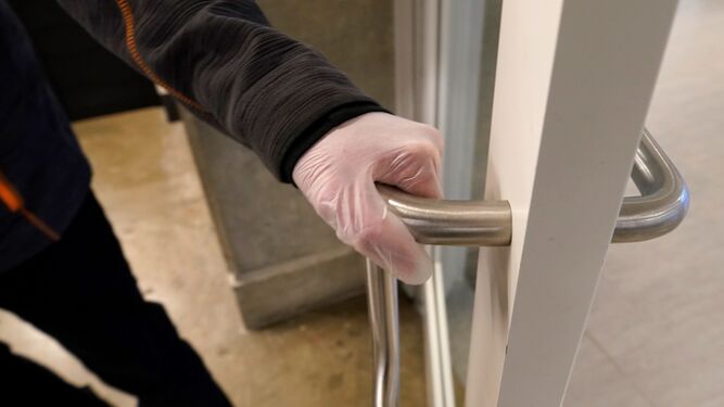 Un hombre abre una puerta con unos guantes desechables puestos.