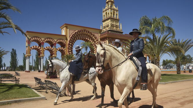 Varios jinetes pasean con sus caballos por delante de la portada de la Feria de 2019.