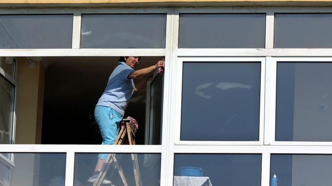 Una empleada de hogar limpia unos ventanales.