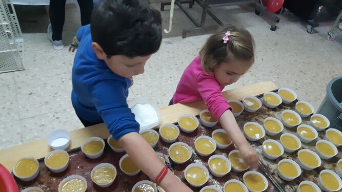 Unos niños echan azúcar sobre unas magdalenas.