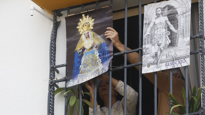 Unos vecinos de Santa Marina colocan en una reja carteles del Resucitado y de la Virgen de la Alegría.