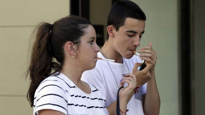Dos jóvenes encienden un cigarrillo.