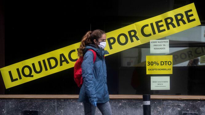 Una joven pasa delante de una tienda cerrada en Córdoba.