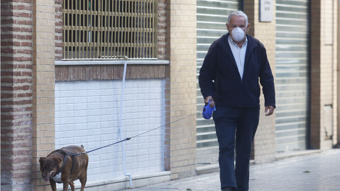 Un hombre protegido con mascarilla saca a pasear a su perro.