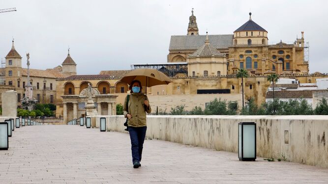 Una mujer pasea bajo un paraguas por el Puente Romano de Córdoba.