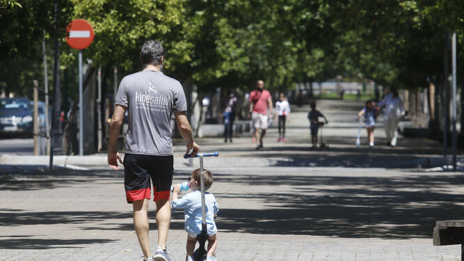 Un hombre pasea con un bebé por una avenida de Córdoba.