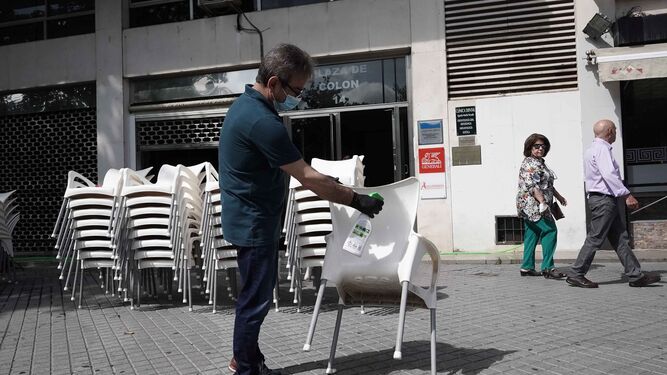 Un hombre prepara su negocio y limpia las sillas para una terraza  en Córdoba.