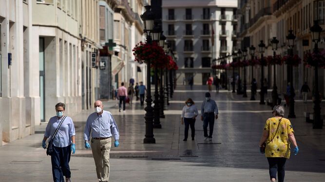 Varias personas pasean por la calle Larios de Málaga protegiéndose con mascarilla.