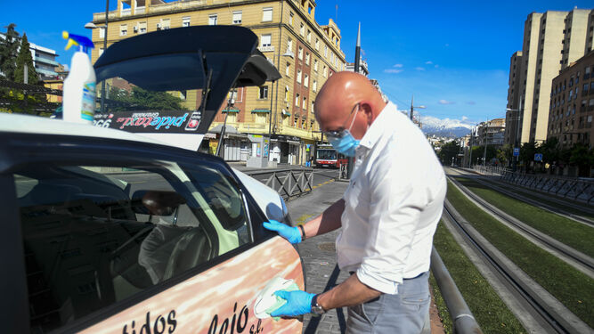 Un taxista con mascarilla limpia su coche.