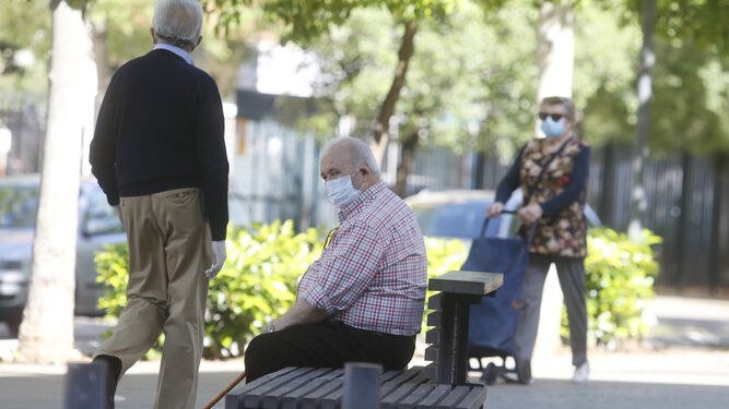 Un hombre descansa en un banco mientras otras dos personas caminan por una avenida de Córdoba.