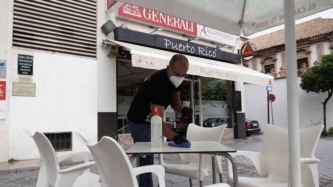 Un camarero limpia la mesa de una terraza con su mascarilla puesta.