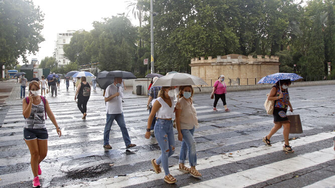 Gente con mascarilla y paraguas cruzan el paso de peatones del Paseo de la Victoria.