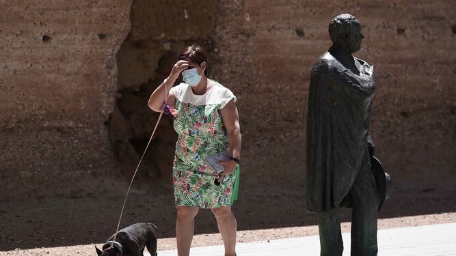 Una mujer con mascarilla pasea a su perro por una plaza de Córdoba.