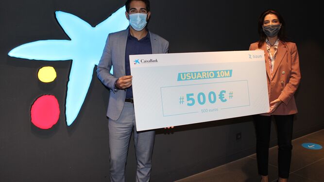 Dos empleados de Caixabank sostienen el cheque regalo del usuario diez millones de Bizum