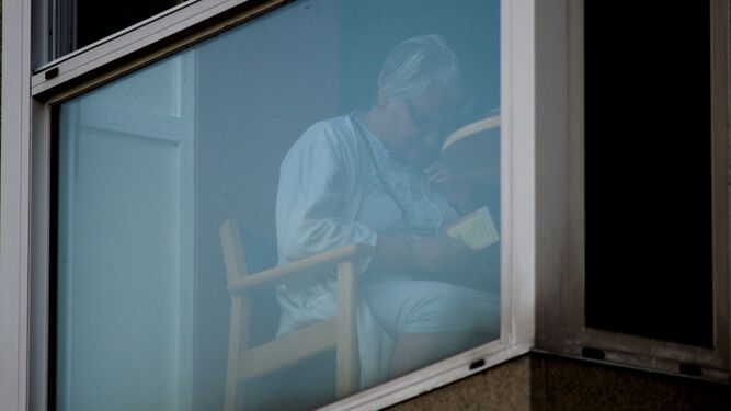 Una usuaria de un centro de mayores lee un libro junto a una ventana.