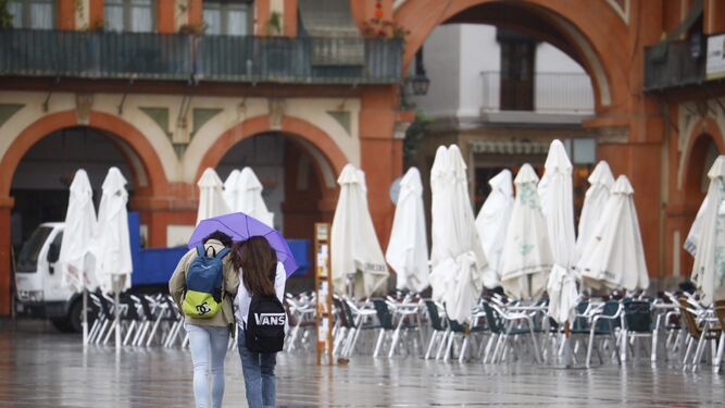 Dos personas caminan bajo la lluvia por la plaza de la Corredera.