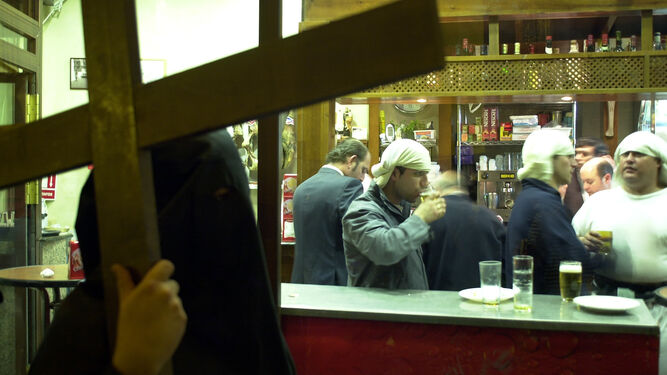 Un penitente pasa por delante de un bar con costaleros dentro.