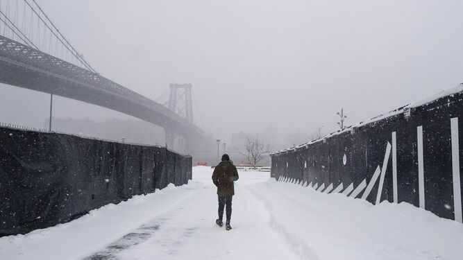 Un hombre camina sobre y bajo la nieve en Brooklyn (Nueva York), hacia el East River y el puente de Williamsburg