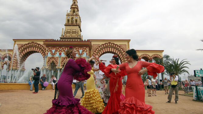 Un grupo de mujeres vestidas de flamenca baila delante de la portada de la Feria.