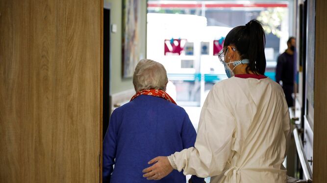 Una profesional sanitaria acompaña a una persona mayor en un centro de mayores.
