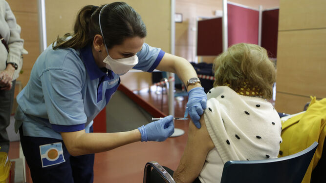 Una profesional sanitaria pone una vacuna a una mujer mayor.