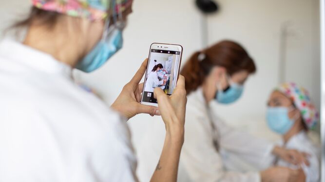 Una enfermera inyecta la vacuna del coronavirus a una compañera mientras otra hace una fotografía.