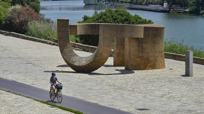 Una ciclista circula por el carril bici junto al río y al monumento de la tolerancia.