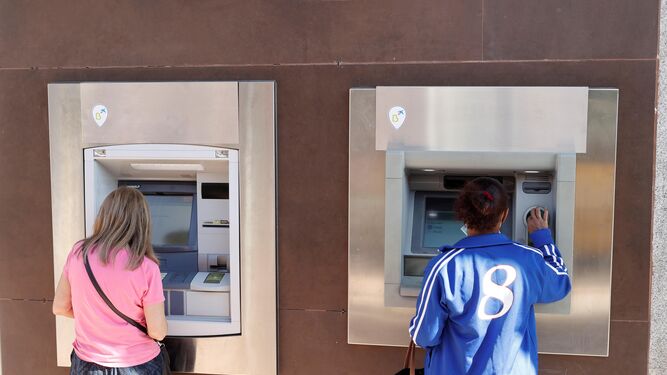 Dos personas sacan dinero de sendos cajeros automáticos